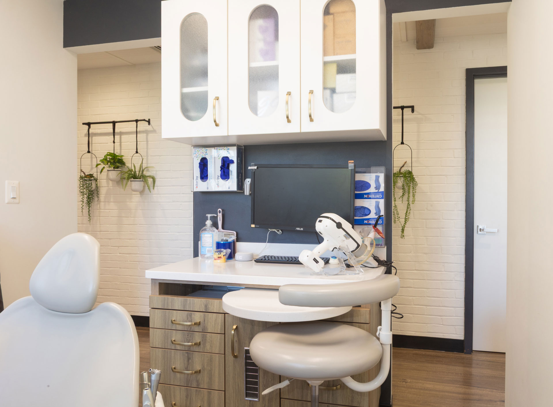 exam room with dental chair and equipment, cabinets, computer and double entrance to hall in the background