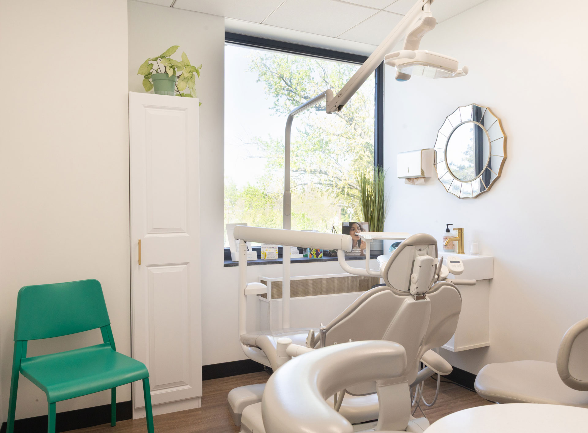 exam room with dental chair and equipment facing window, mirror and sink on right wall, green chair on left