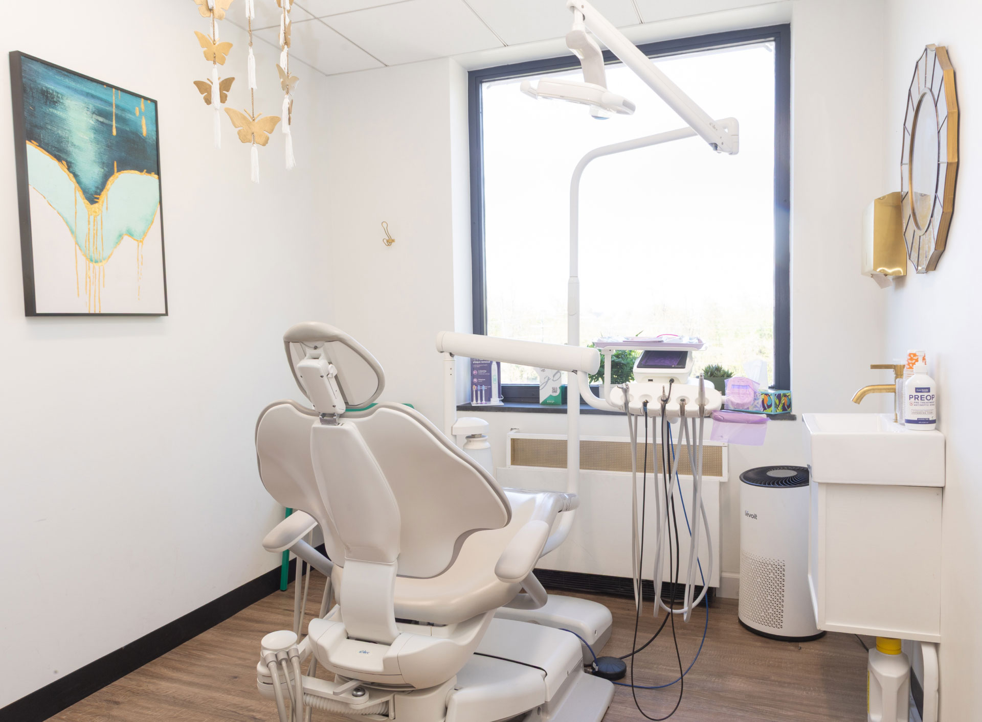 exam room with dental chair and equipment facing window, mirror and sink on right wall, artwork on left wall and butterfly mobile hanging from ceiling