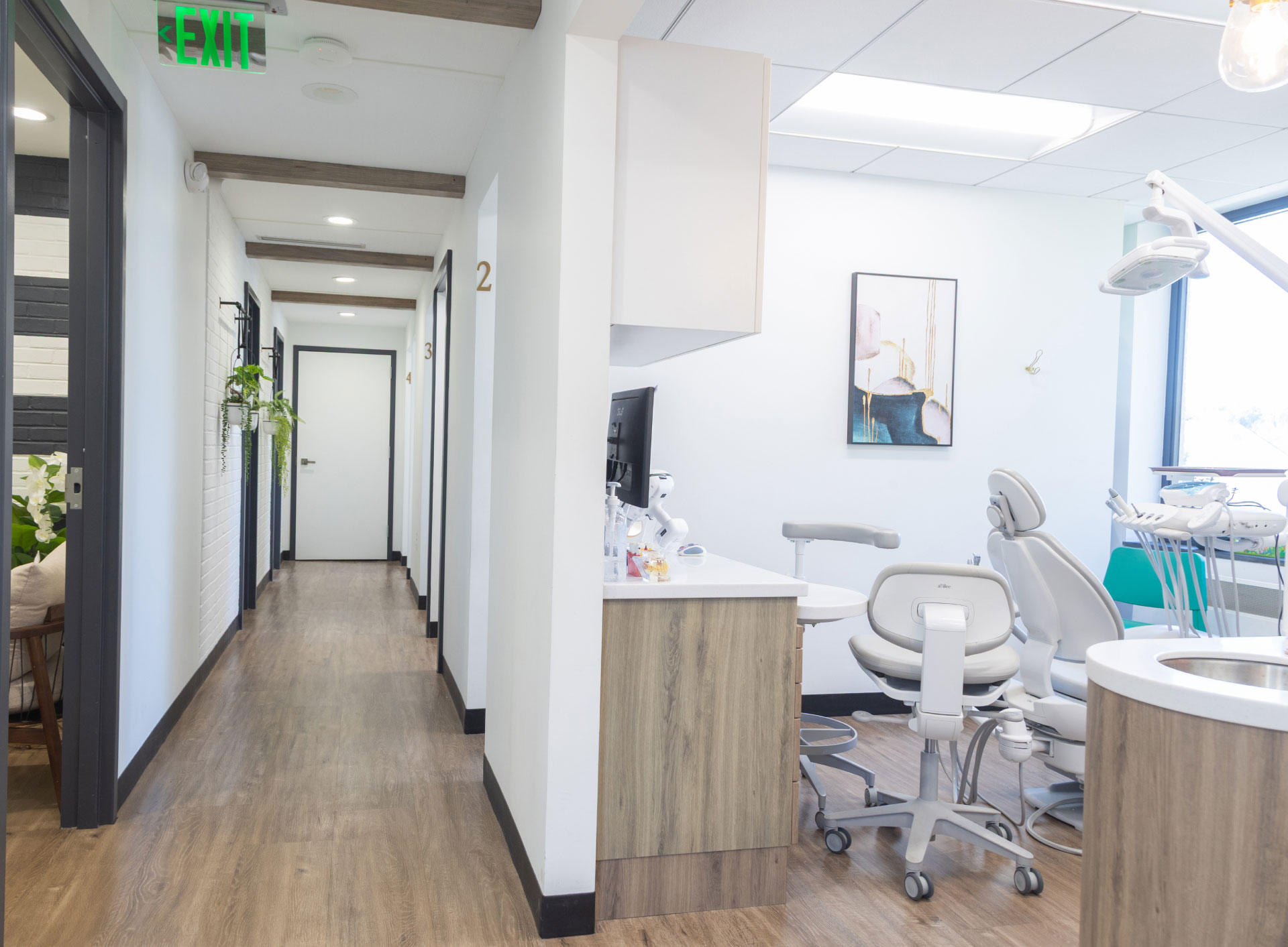 exam room with dental chair and equipment on right and long hallway on left with wood beams on ceiling, plants hanging from wall, entrances to exam rooms