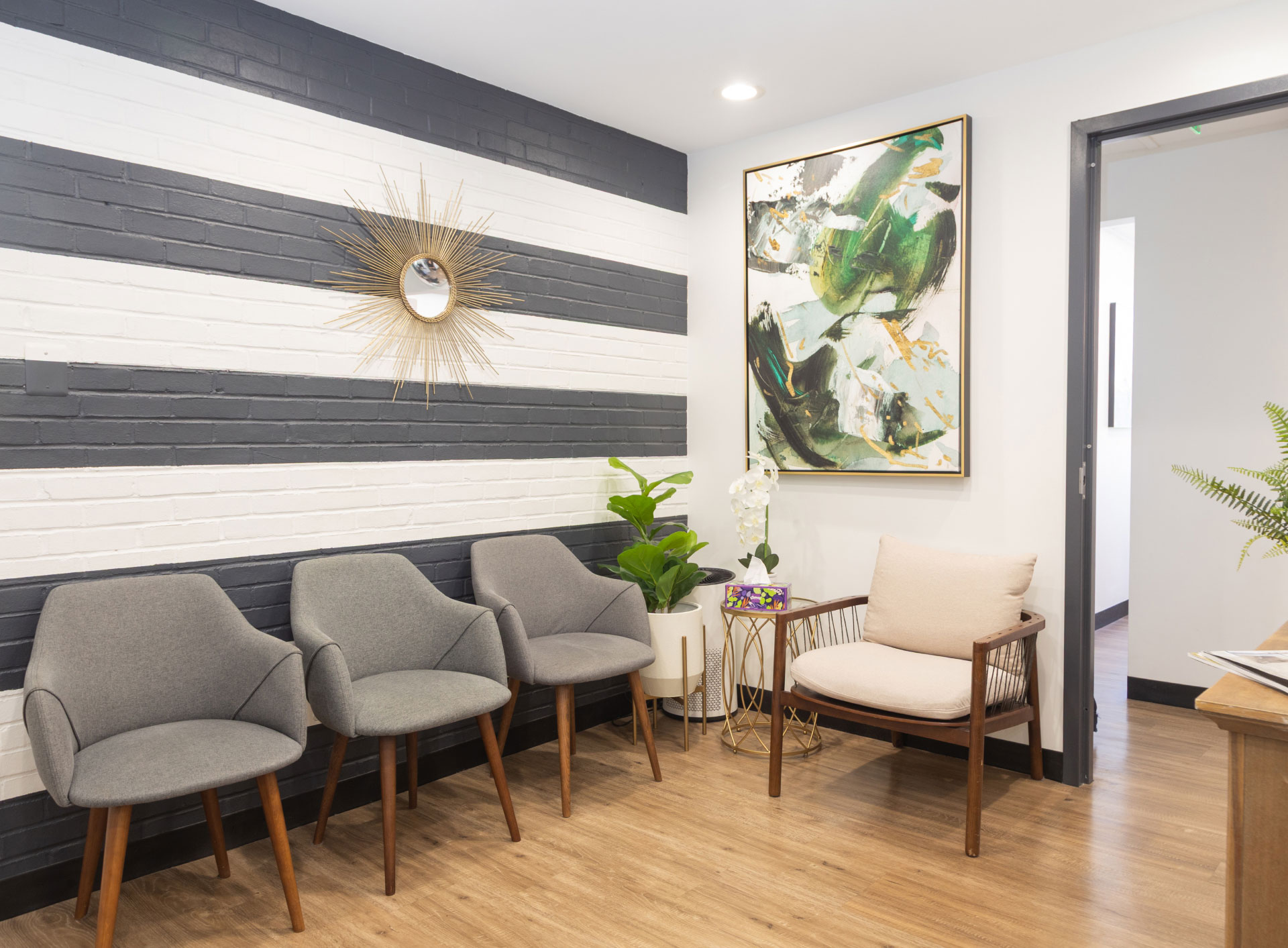 reception area with gray and tan chairs for seating lined up against brick wall painted with horizontal gray and white stripes