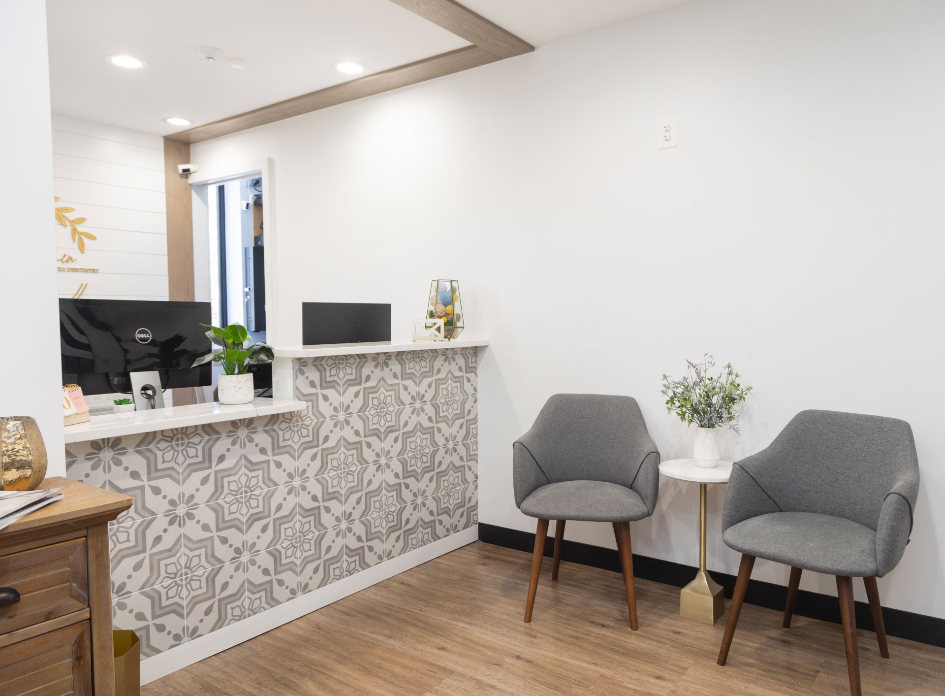 front desk with patterned tile on front with two gray upholstered chairs and side table in between